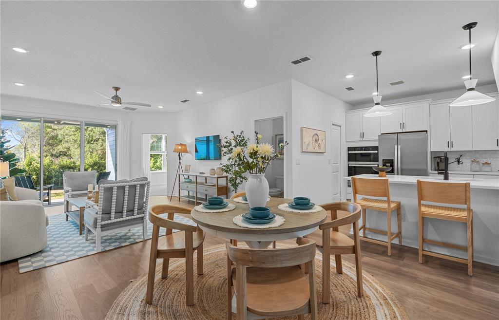 An open-concept kitchen and dining area with light wood floors and white cabinetry — 212 MISTY HARBOR TRACE, PALM COAST, FL