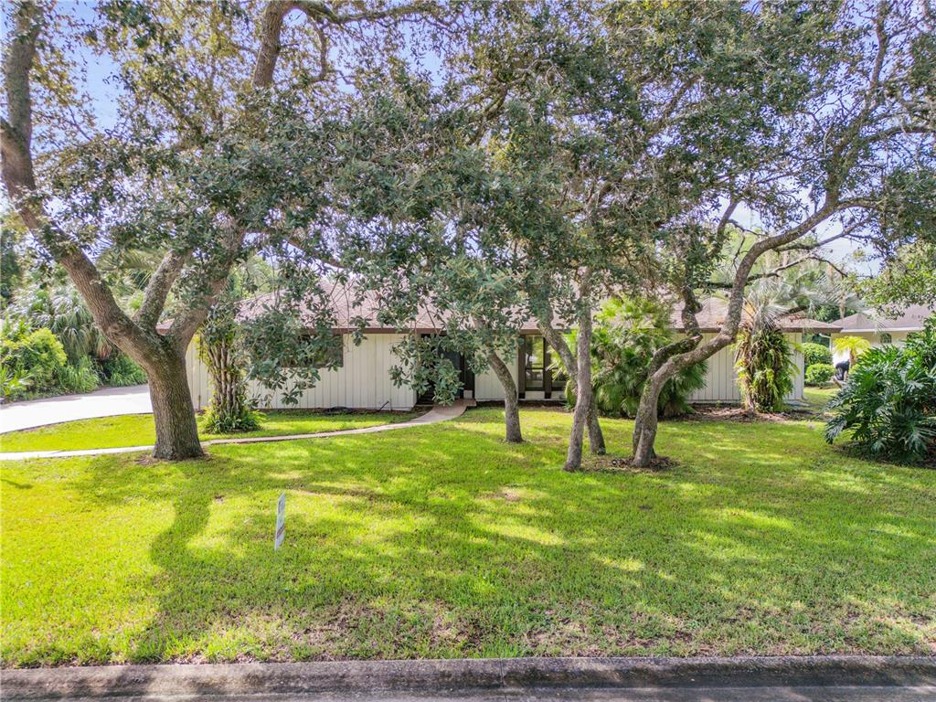 A single-story house with vertical siding is partially obscured by large oak trees — 530 CLUB HOUSE BOULEVARD, NEW SMYRNA BEACH, FL