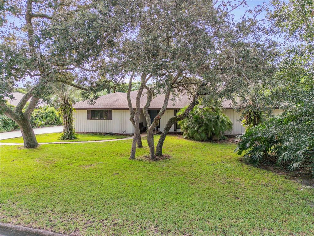 A single-story house with light-colored siding is surrounded by large trees and a green lawn — 530 CLUB HOUSE BOULEVARD, NEW SMYRNA BEACH, FL