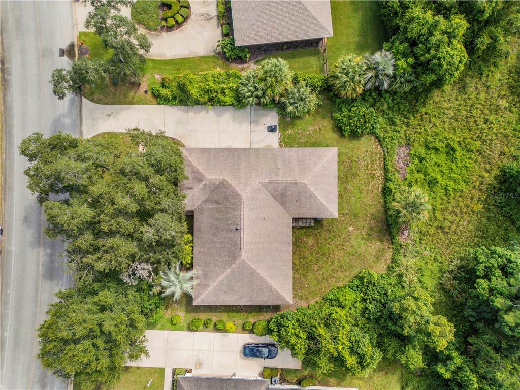 An aerial view shows a house with a gray roof, a driveway, and surrounding trees — 530 CLUB HOUSE BOULEVARD, NEW SMYRNA BEACH, FL