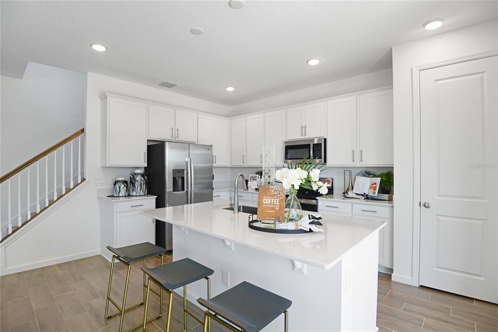 A modern kitchen features white cabinetry, a central island with a sink, and sliding glass doors — 172 FLAG LILLY LANE, UMATILLA, FL