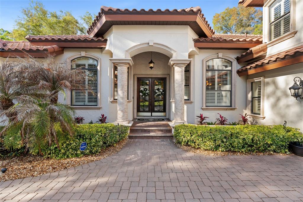 A paved walkway leads to the arched entryway of a stucco home with tiled roofing — 7341 BELLA FORESTA PLACE, SANFORD, FL