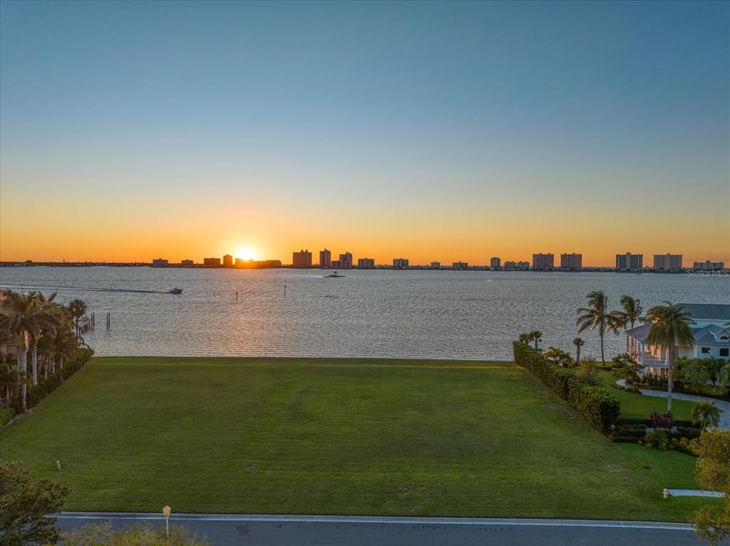 A vacant waterfront lot overlooks a bay with a distant city skyline at sunset — ST ANDREWS DRIVE, BELLEAIR, FL