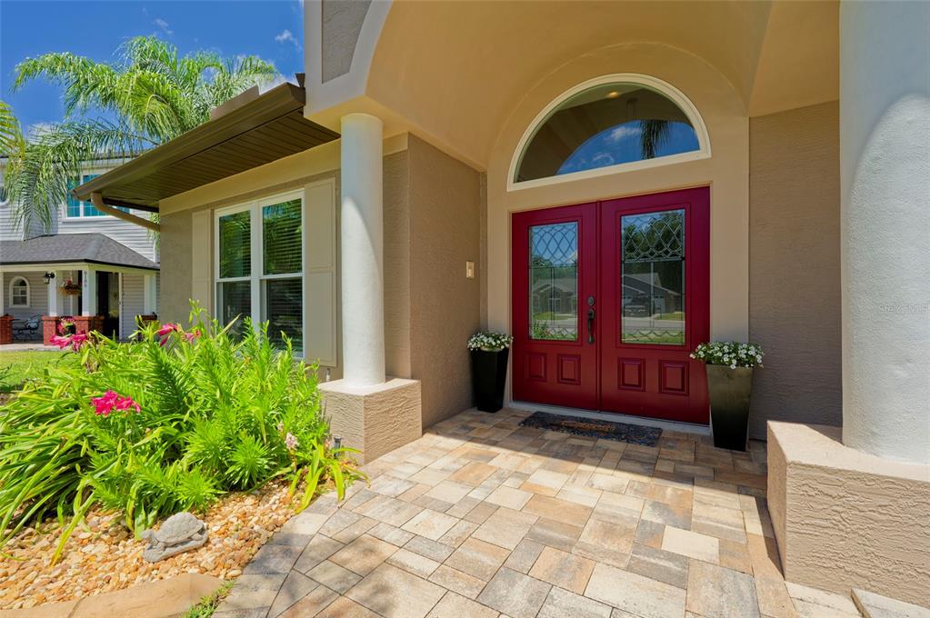 A red double front door with a transom window sits under a covered entryway — 8115 MONTOCK COURT, TRINITY, FL