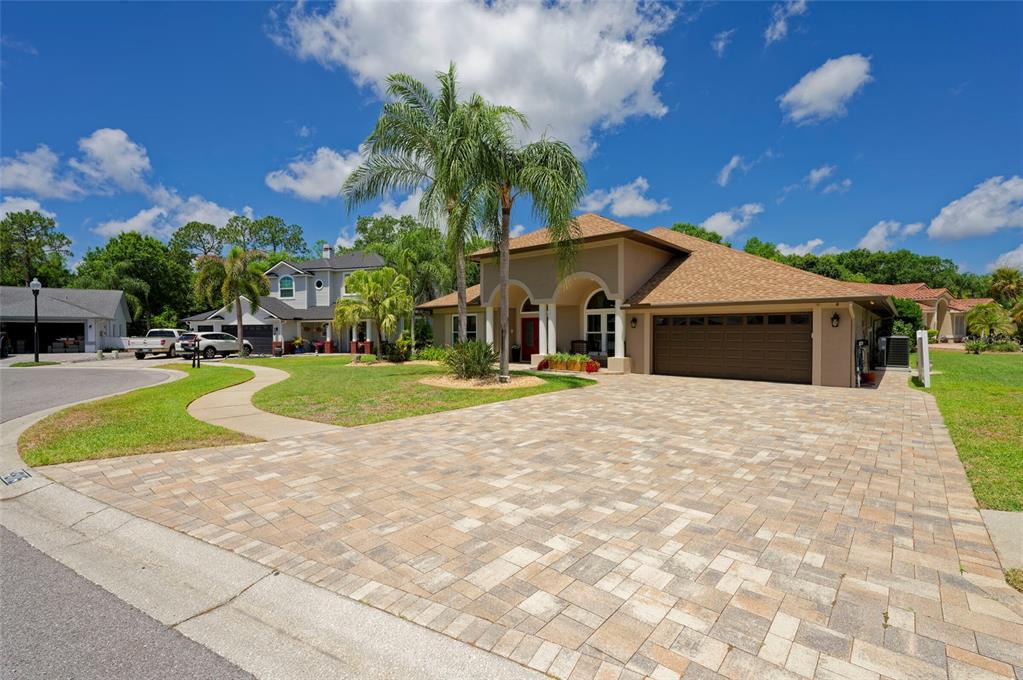 A tan house with a brown roof and a large paver driveway under a blue sky — 8115 MONTOCK COURT, TRINITY, FL