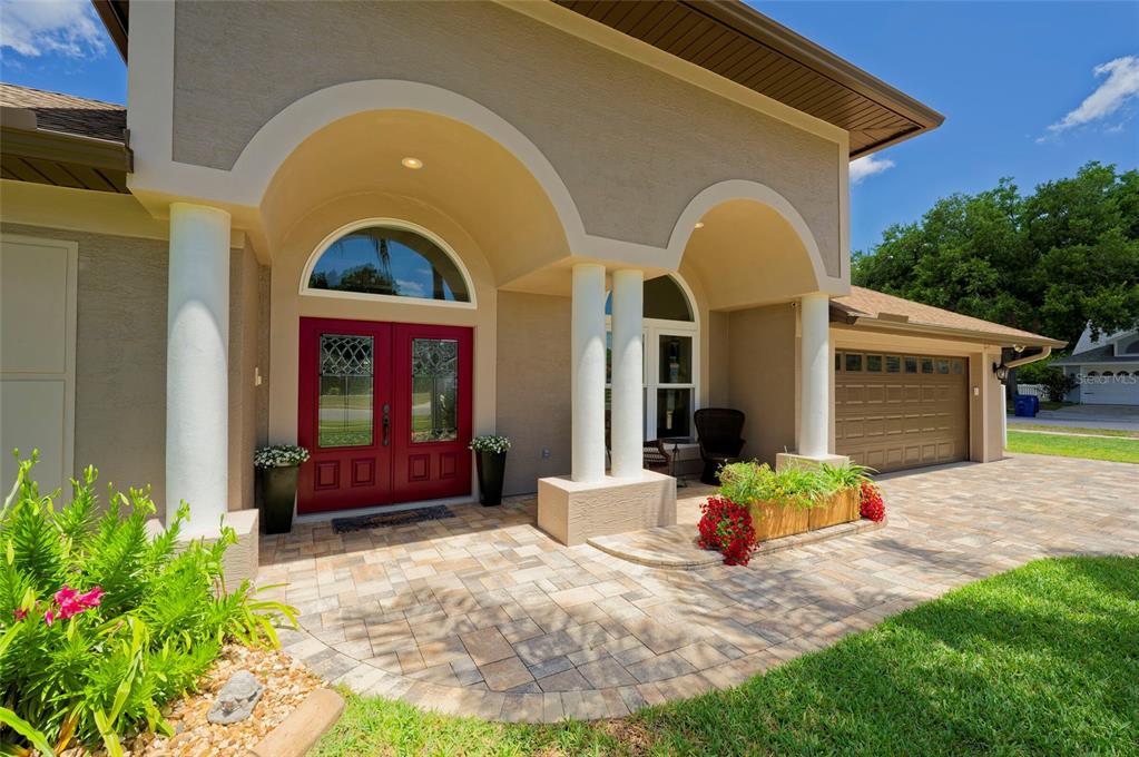 The exterior of a house features a paved entryway, white columns, and a red double door — 8115 MONTOCK COURT, TRINITY, FL