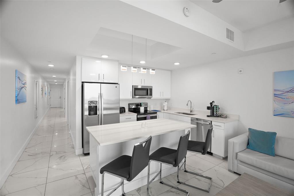 A modern kitchen with white cabinets, stainless steel appliances, and a central island with seating — 11500 GULF BOULEVARD UNIT 603, TREASURE ISLAND, FL