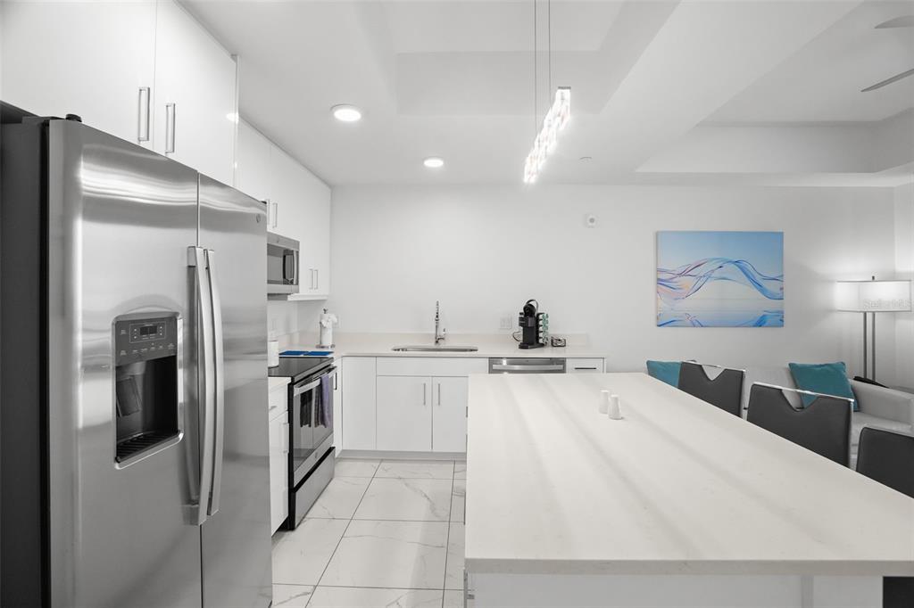 A modern kitchen features white cabinetry, stainless steel appliances, and a large white island — 11500 GULF BOULEVARD UNIT 603, TREASURE ISLAND, FL