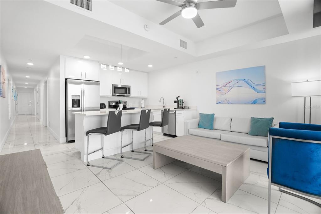 A modern open-concept living room and kitchen with white cabinetry, stainless appliances, and marble flooring — 11500 GULF BOULEVARD UNIT 603, TREASURE ISLAND, FL