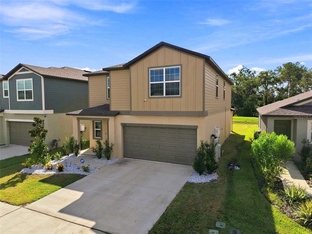 A two-story suburban house with a tan exterior, a two-car garage, and a concrete driveway — 35418 ACKLEY TRACE, ZEPHYRHILLS, FL