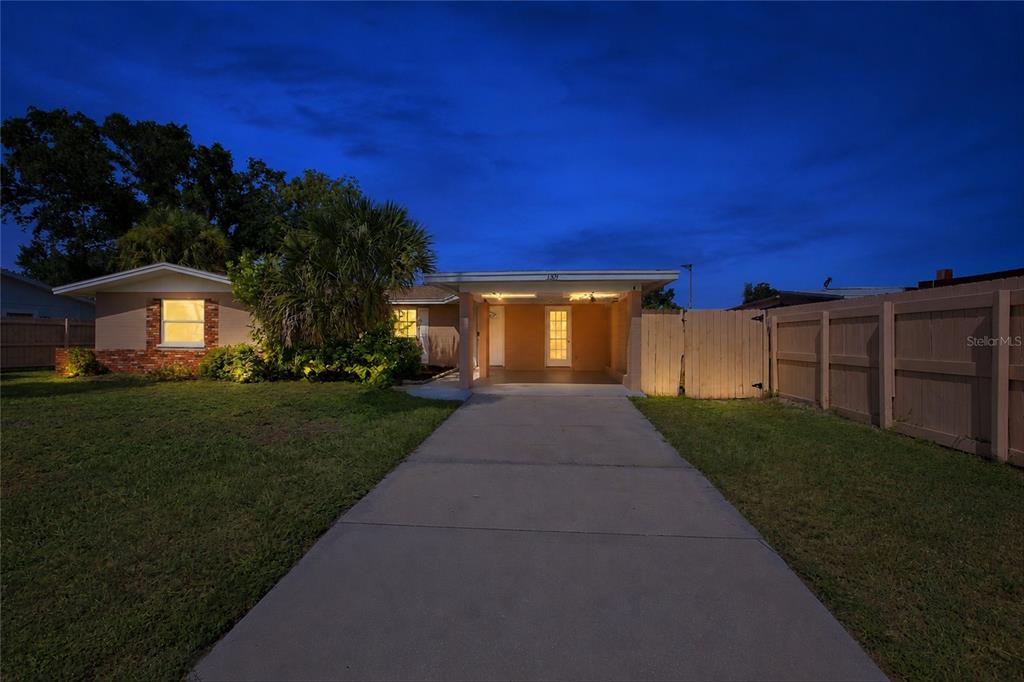 A single-story house with a concrete driveway, a carport, and a wooden privacy fence at dusk — 1509 BANYAN DRIVE, VENICE, FL