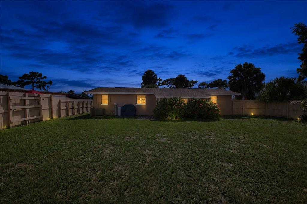 The exterior of a single-story house at dusk features a grassy backyard and wooden fencing — 1509 BANYAN DRIVE, VENICE, FL