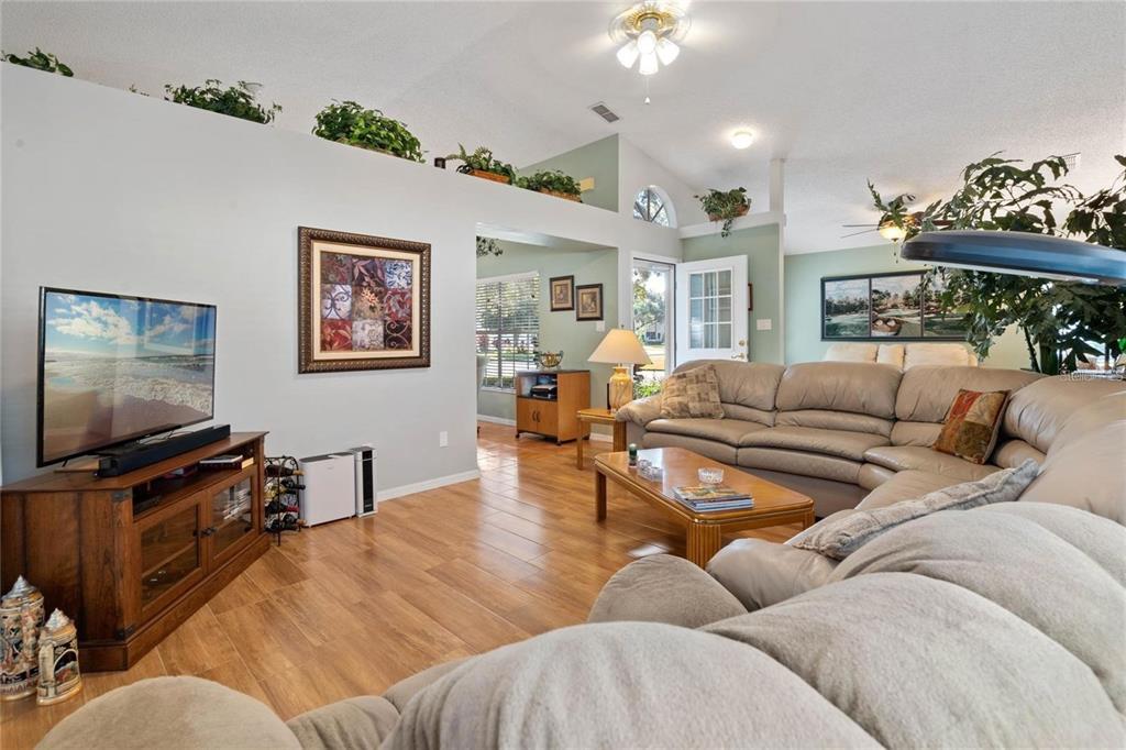 A living room features a large sectional sofa, a television on a wooden stand, and plants — 25300 HIBISCUS STREET, LEESBURG, FL