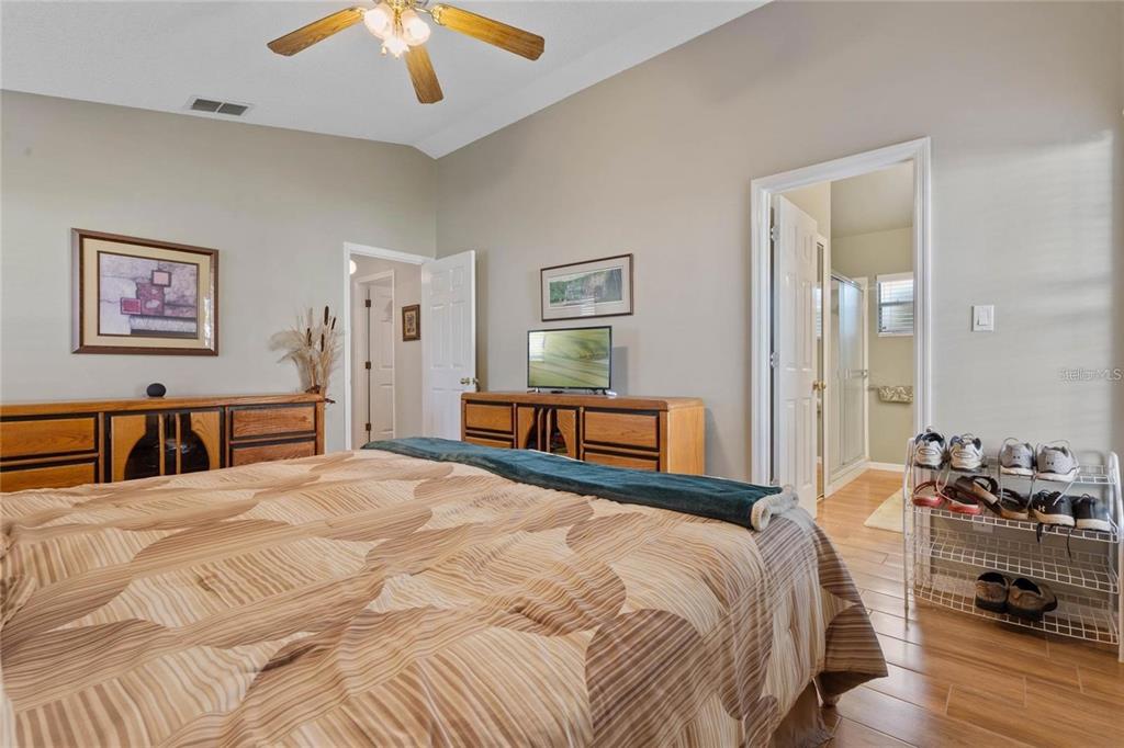 A bedroom features a bed with a patterned comforter, two wooden dressers, and a shoe rack — 25300 HIBISCUS STREET, LEESBURG, FL