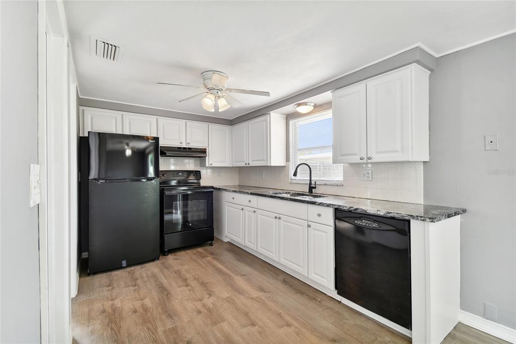 A kitchen features white cabinets, black appliances, a dark countertop, and wood-look flooring — 7721 ARBORDALE DRIVE, PORT RICHEY, FL