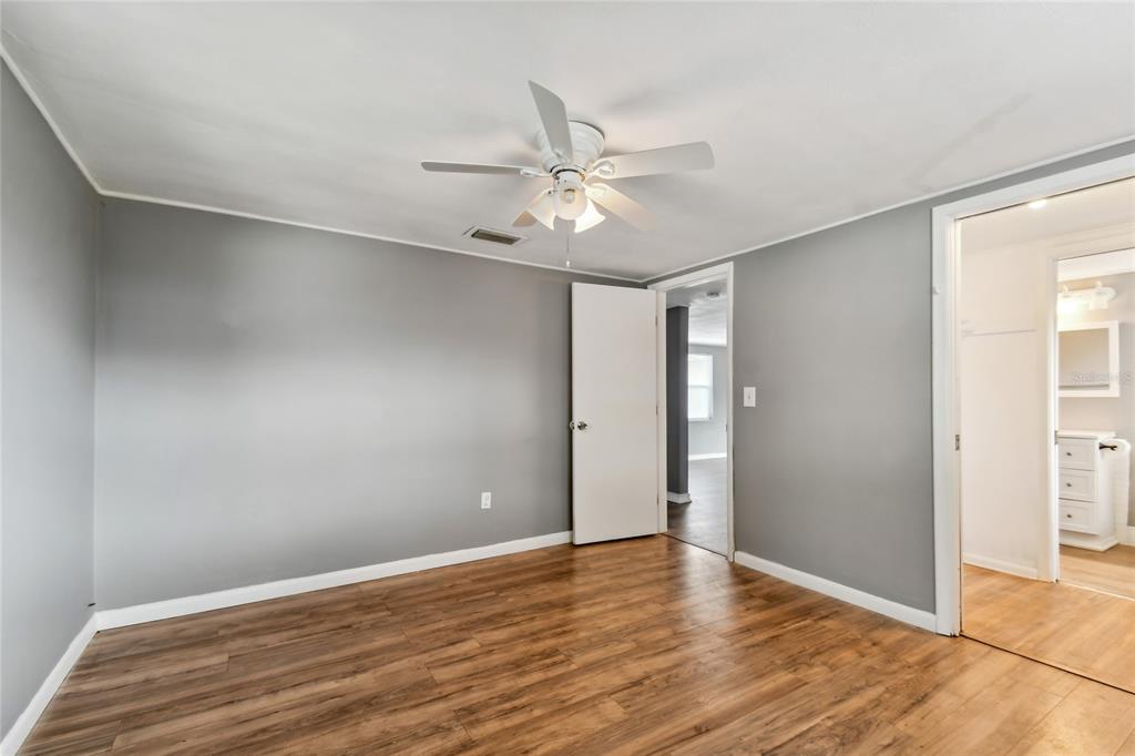 A bedroom with gray walls, wood-look flooring, a ceiling fan, and an attached bathroom — 7721 ARBORDALE DRIVE, PORT RICHEY, FL