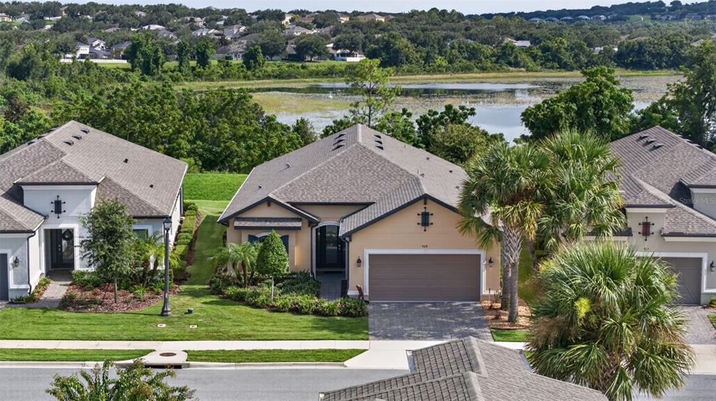 An elevated view shows three suburban houses with gray roofs and a lake in the background — 908 BRAEWOOD DRIVE, CLERMONT, FL