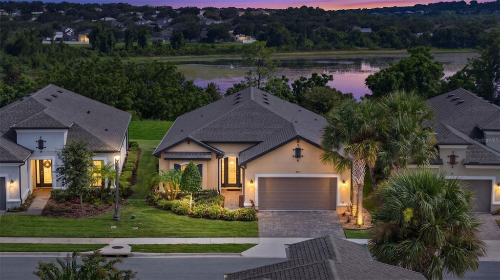 An aerial view of a suburban house with a garage, palm trees, and a lake — 908 BRAEWOOD DRIVE, CLERMONT, FL