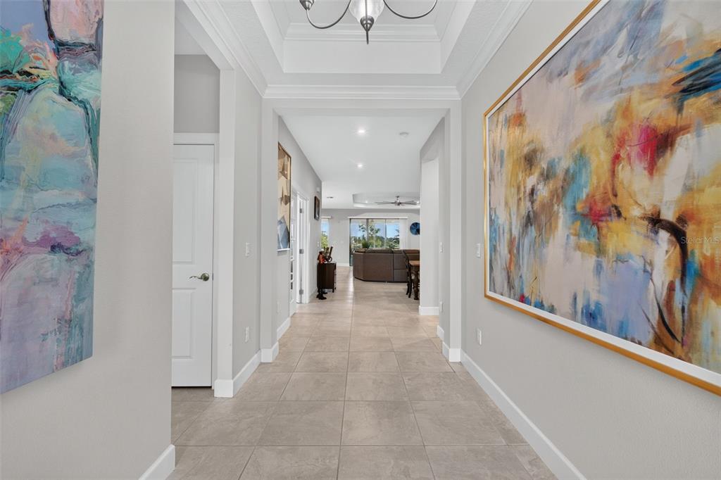 A tiled hallway leads from a foyer toward an open-concept living area with tray ceilings — 908 BRAEWOOD DRIVE, CLERMONT, FL