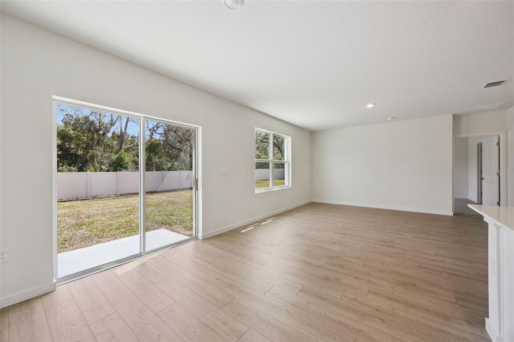 An empty living room with light wood-look flooring, sliding glass doors, and a backyard view — 1103 GULL DRIVE, APOPKA, FL