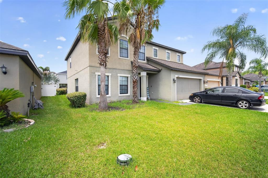 A two-story suburban house with a tan stucco exterior, a garage, and palm trees — 11202 CARRICK STONE STREET, WIMAUMA, FL