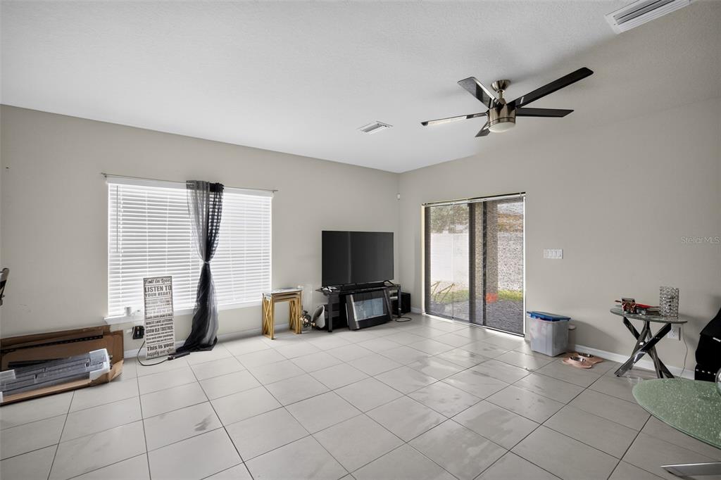 A living room features light-colored tile flooring, a ceiling fan, a television, and sliding glass doors — 11202 CARRICK STONE STREET, WIMAUMA, FL