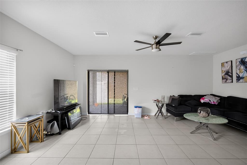 A living room features light tile floors, a black sectional sofa, and a sliding glass door — 11202 CARRICK STONE STREET, WIMAUMA, FL