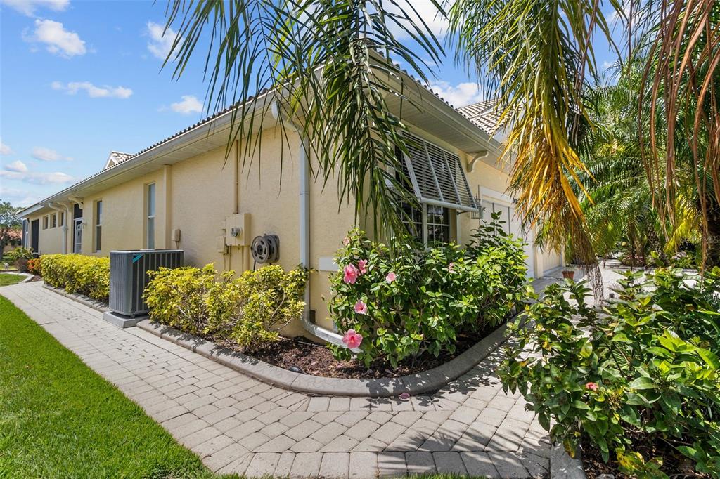 A side view of a yellow house with a paver walkway and landscaping — 9486 HAWK NEST LANE, NORTH PORT, FL