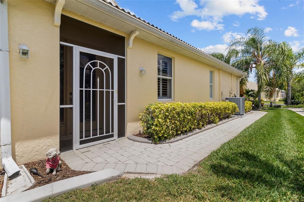 A yellow house exterior features a screened door, a paver walkway, and a landscaped hedge — 9486 HAWK NEST LANE, NORTH PORT, FL