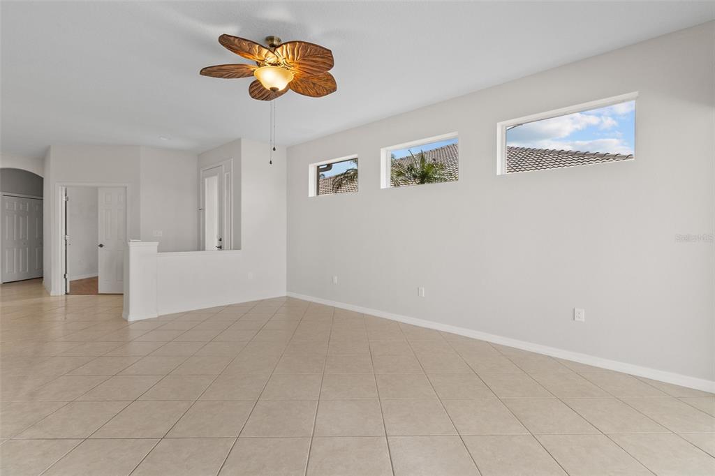 An empty room with light-colored tile flooring, a tropical-style ceiling fan, and three high windows — 9486 HAWK NEST LANE, NORTH PORT, FL