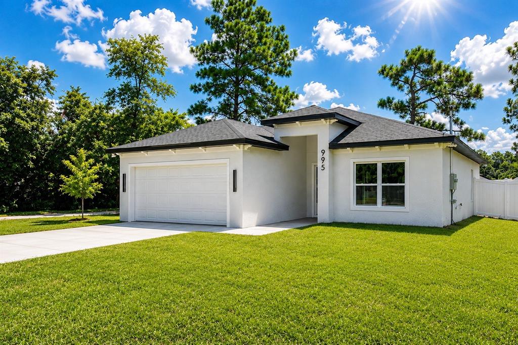 A single-story house with a dark garage door, white stucco walls, and a lit entryway — 995 9TH AVENUE, DELAND, FL