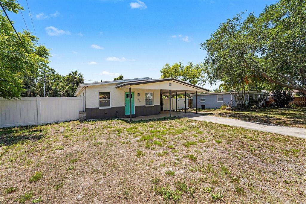 A single-story house with a carport, a teal front door, and a white privacy fence — 9346 89TH AVE, SEMINOLE, FL
