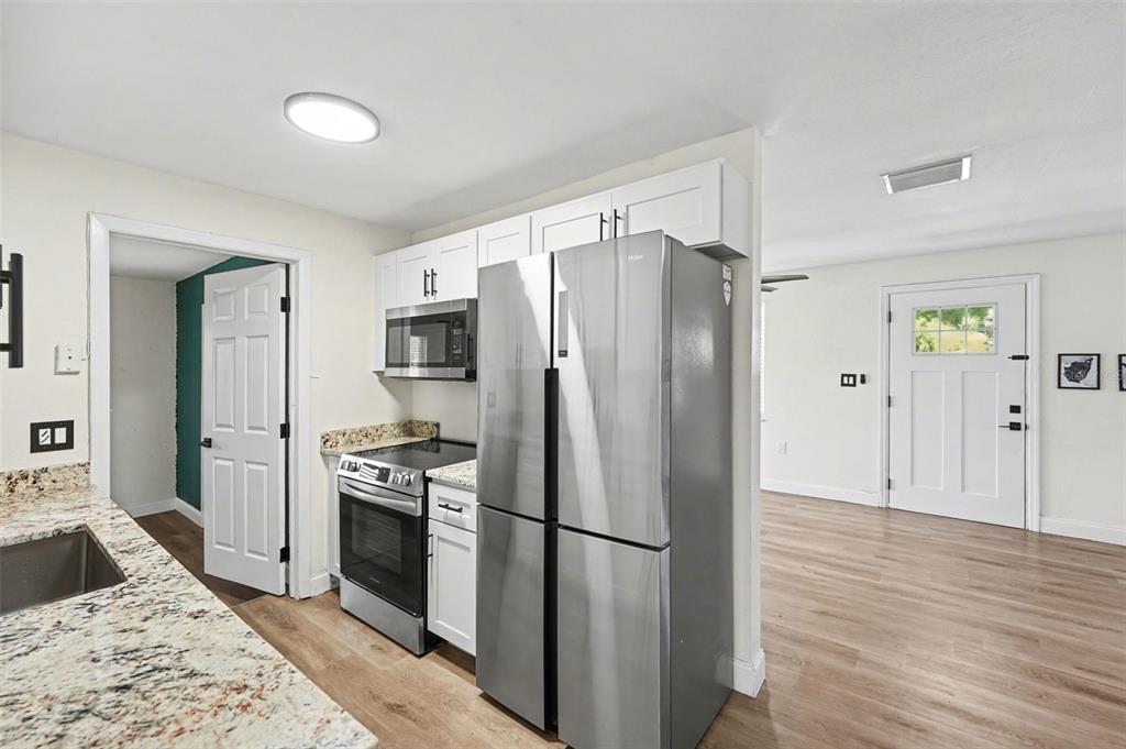 A kitchen with stainless steel appliances and white cabinets opens into a living area — 9346 89TH AVE, SEMINOLE, FL