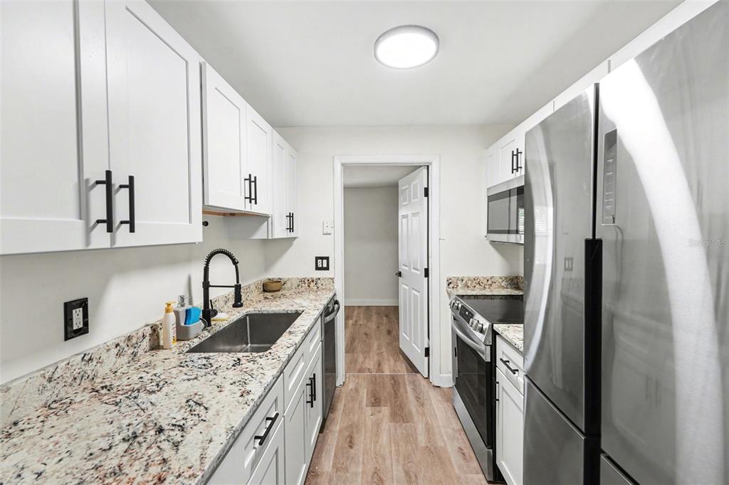 A galley kitchen features white cabinets, granite countertops, stainless steel appliances, and wood-look flooring — 9346 89TH AVE, SEMINOLE, FL