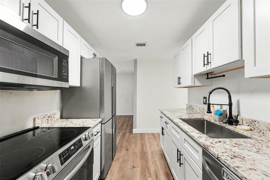 A galley kitchen features white cabinets, stainless steel appliances, and granite countertops — 9346 89TH AVE, SEMINOLE, FL