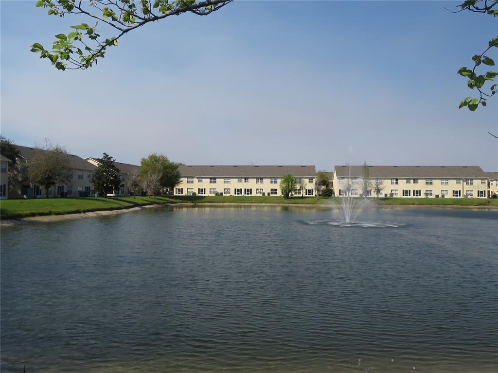 A pond with a fountain sits in front of two-story apartment buildings under a blue sky — 2806 CLUB CORTILE CIRCLE UNIT B, KISSIMMEE, FL