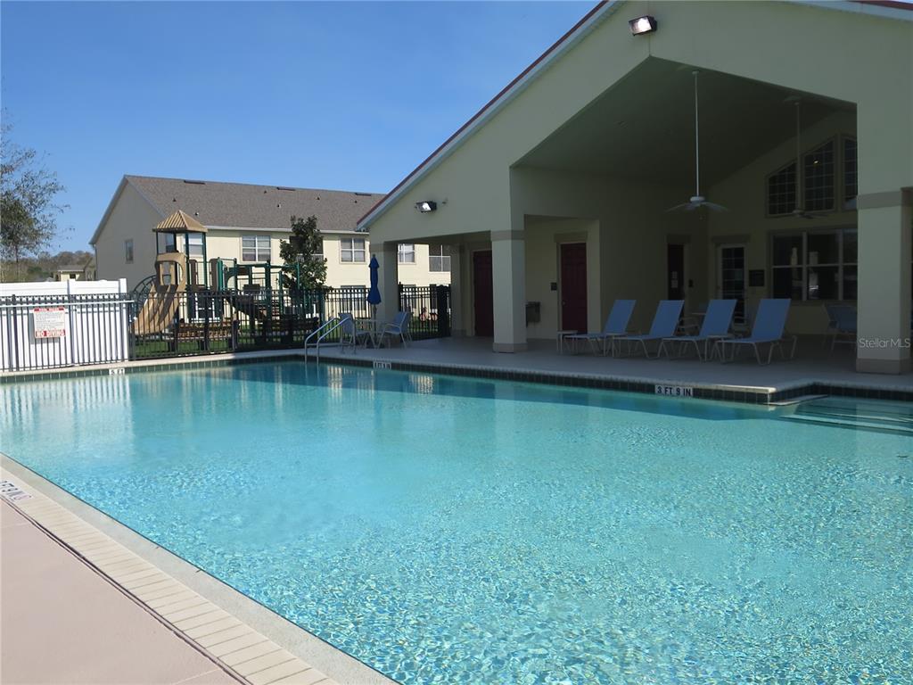 A swimming pool sits in front of a community clubhouse with a covered patio and playground — 2806 CLUB CORTILE CIRCLE UNIT B, KISSIMMEE, FL