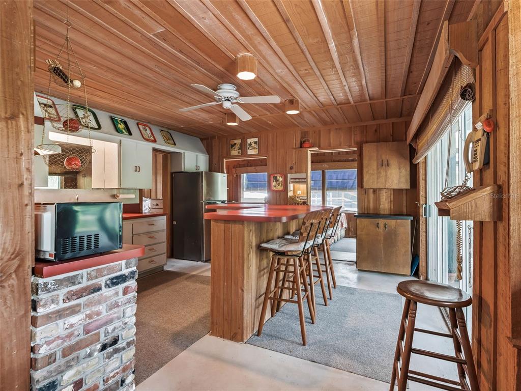 A rustic kitchen features wood-paneled walls and ceiling, a red breakfast bar, and bar stools — 10518 SW 64TH AVENUE, BUSHNELL, FL