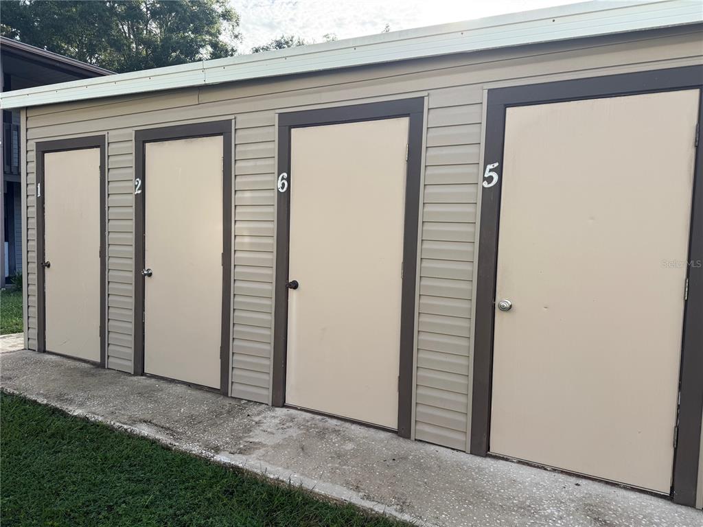 A row of four numbered storage unit doors with tan siding on a concrete walkway — 11616 BAYWOOD MEADOWS DRIVE UNIT 2, NEW PORT RICHEY, FL