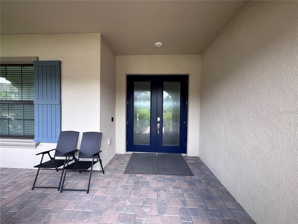 A covered entryway features a blue double door, two black chairs, and paver flooring — 28661 PICANA LANE, WESLEY CHAPEL, FL