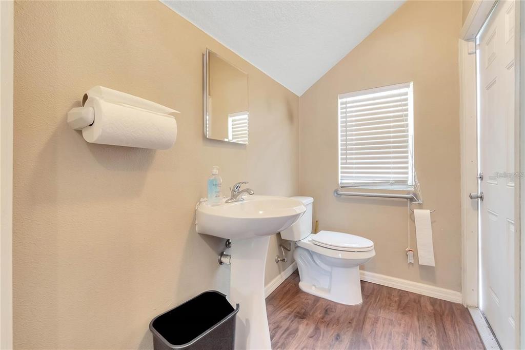 A small bathroom features a pedestal sink, a toilet, a mirror, and wood-look flooring — 8440 COUNTY ROAD 48, YALAHA, FL