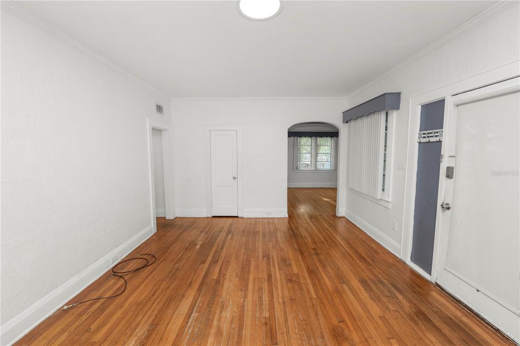 An empty room features hardwood floors, white walls, an arched doorway, and a front door — 1220 RUBY STREET, LAKELAND, FL