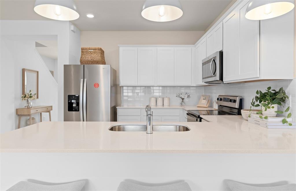 A kitchen features white cabinets, stainless steel appliances, and a quartz-topped island with a sink — 15516 PEACEFUL PINES ALLEY, CLERMONT, FL
