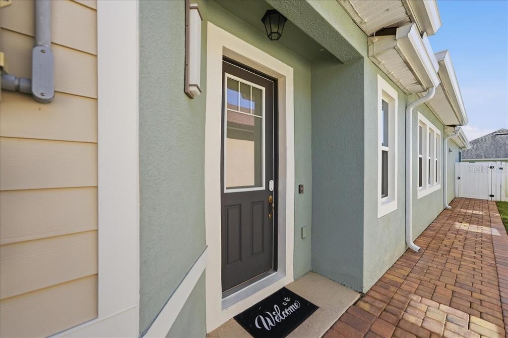 A side entrance with a dark door, a welcome mat, and a brick walkway — 2524 RAPOLLO DRIVE, KISSIMMEE, FL