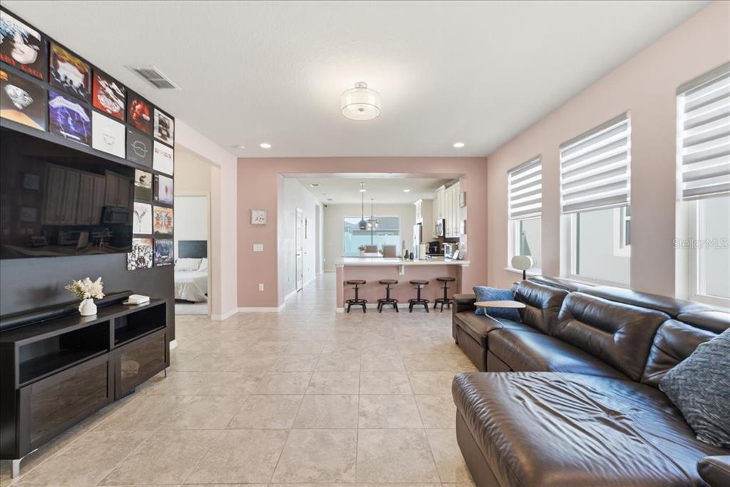 A living room with a large television, wall-mounted album art, and an open kitchen beyond — 2524 RAPOLLO DRIVE, KISSIMMEE, FL
