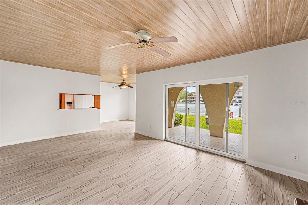 A living room with wood-look tile floors, a wood-paneled ceiling, and sliding glass doors — 546 PLAZA SEVILLE COURT UNIT 85, TREASURE ISLAND, FL