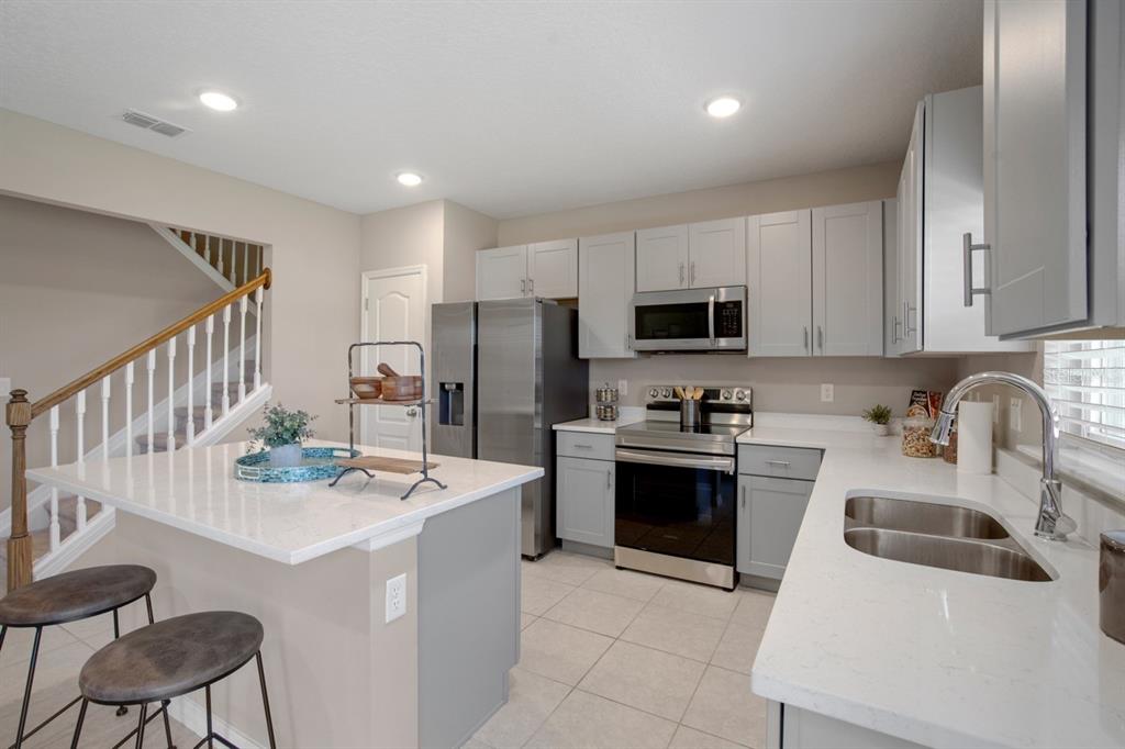 A modern kitchen features light gray cabinets, stainless steel appliances, and a white quartz island — 314 BOWFIN LANE, POINCIANA, FL
