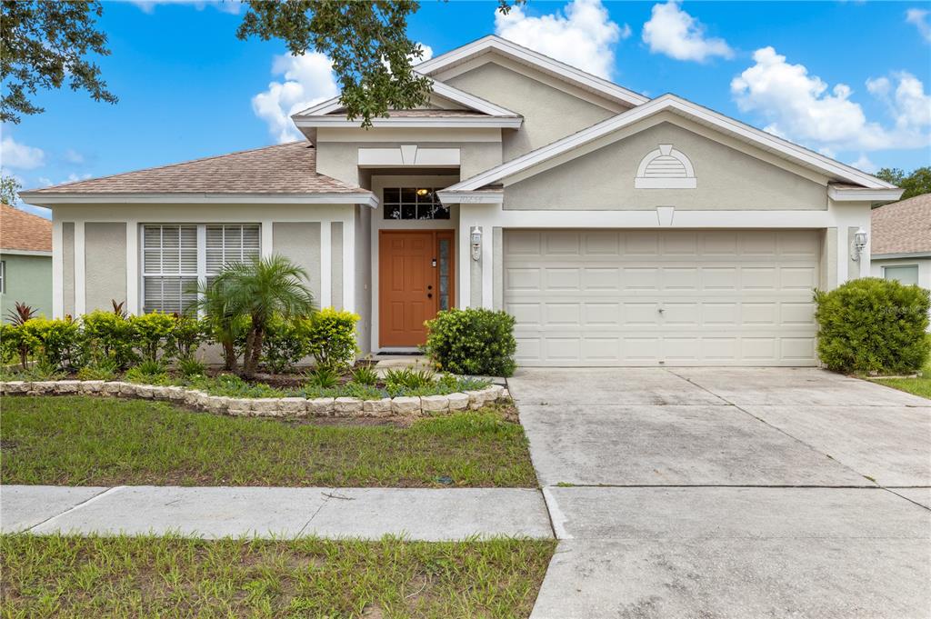A single-story suburban house with a beige stucco exterior, a two-car garage, and a driveway — 10234 HUNTERS HAVEN BOULEVARD, RIVERVIEW, FL
