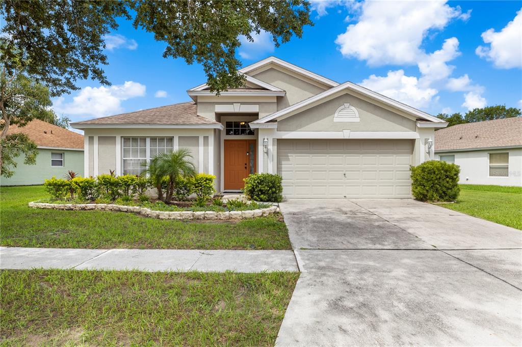 A single-story suburban house with a tan stucco exterior, a two-car garage, and a front lawn — 10234 HUNTERS HAVEN BOULEVARD, RIVERVIEW, FL