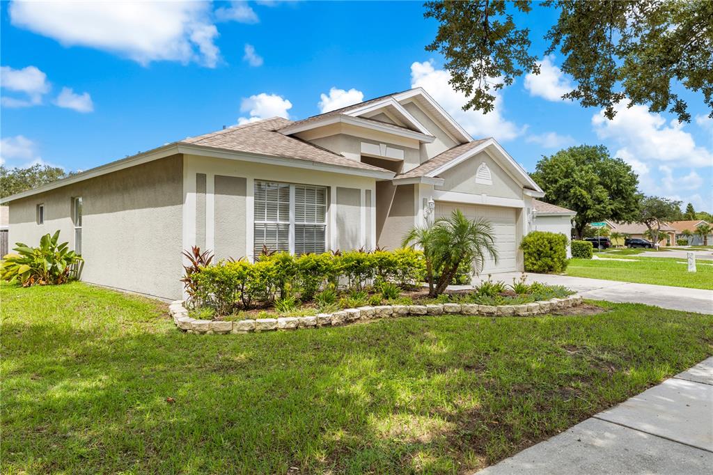 A single-story suburban house with a tan stucco exterior, a two-car garage, and landscaped yard — 10234 HUNTERS HAVEN BOULEVARD, RIVERVIEW, FL